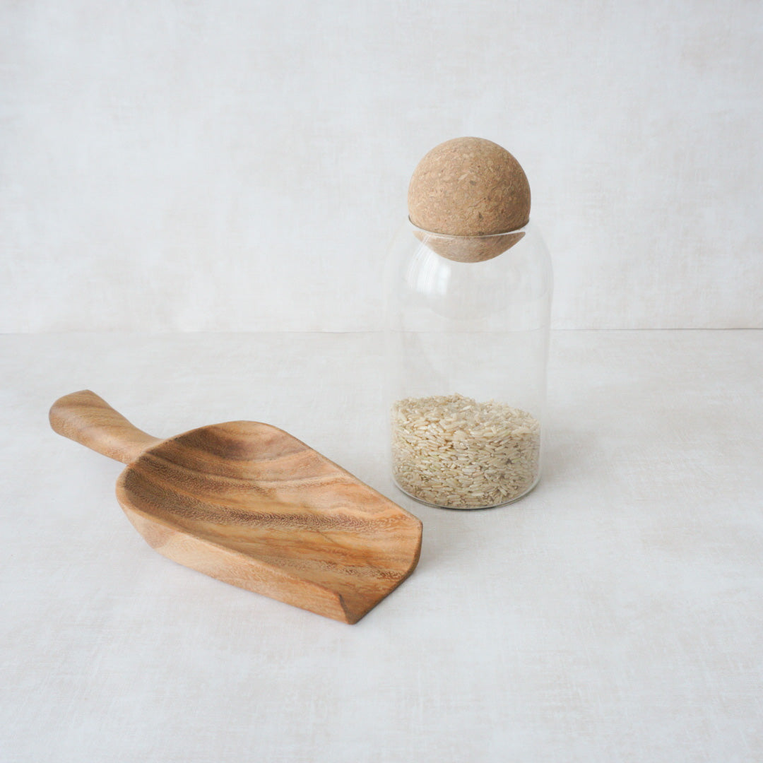 Glass kitchen storage cannister with rice inside and a wood scoop